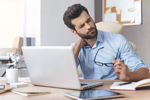 Mann mit Muskelschmerzen sitzt vor dem Taptop